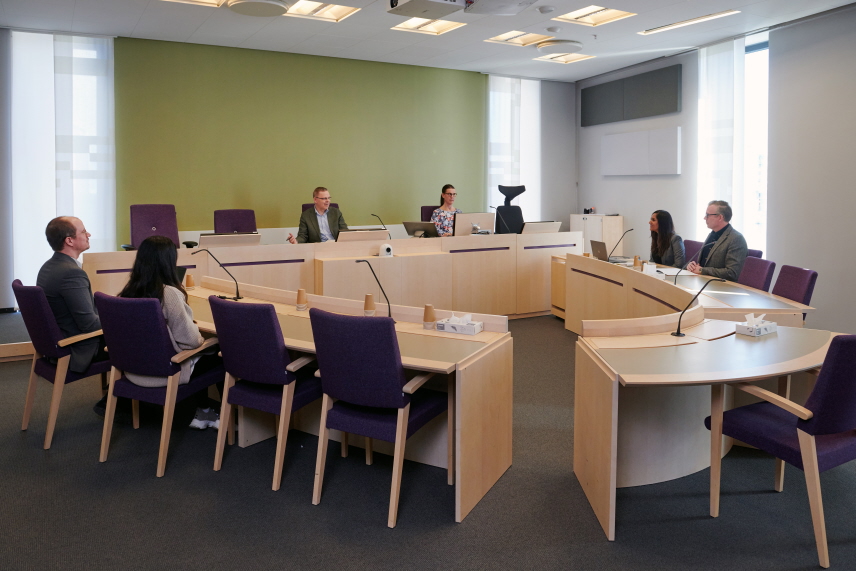 Rättegångssal med parter och deras ombud samt domare och protokollförare