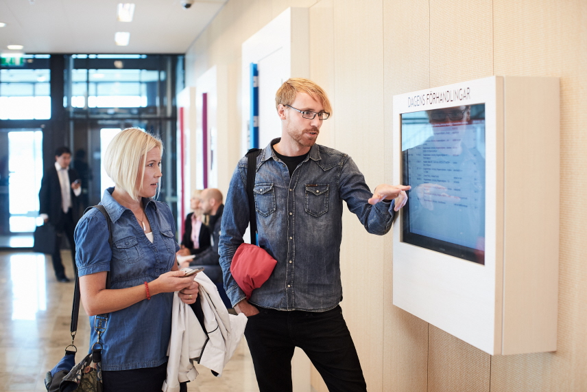 Två personer står vid en skärm som visar dagens förhandlingar i domstolen. Foto.